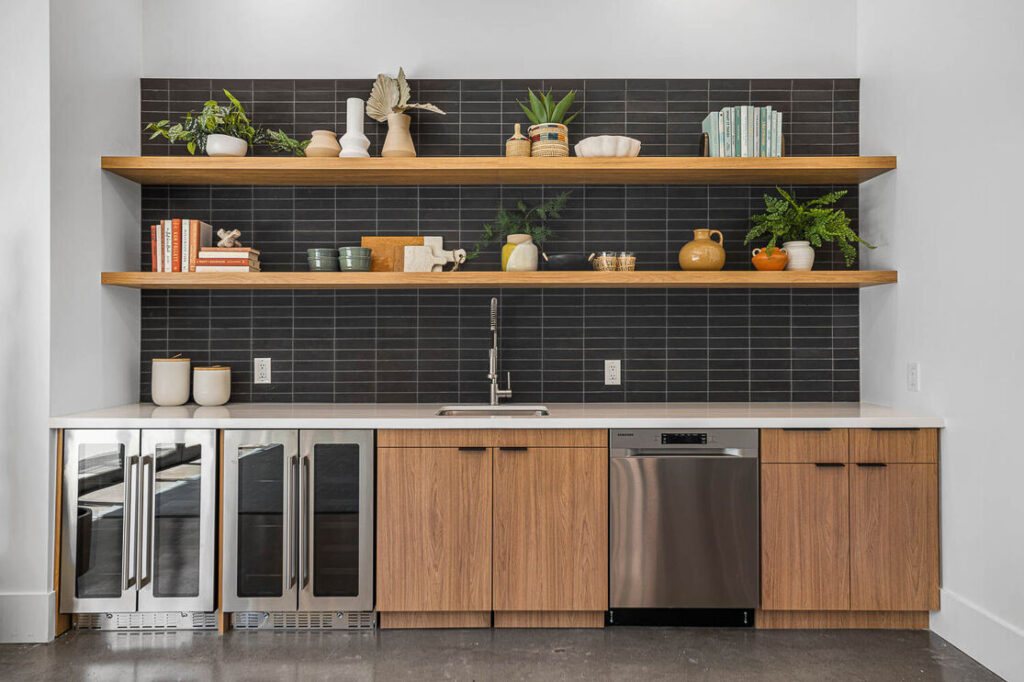 The clubhouse kitchen with two shelves of decor and 2 beverage chiller adn one mini fridge with a sink and white countertops