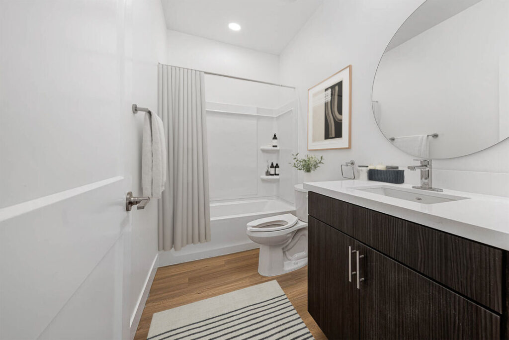 bathroom with dark brown cabinets and bathtub, large circle mirror and one sink and toilet