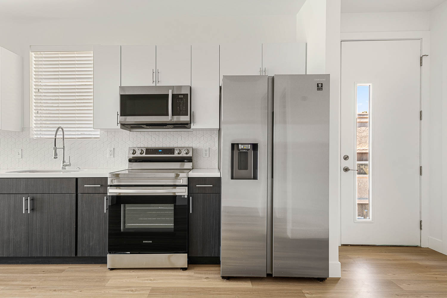 Kitchen with stainless steel appliances. Refrigerator and dark grey cabinets on the bottom, white cabinet above the counter, entrance door