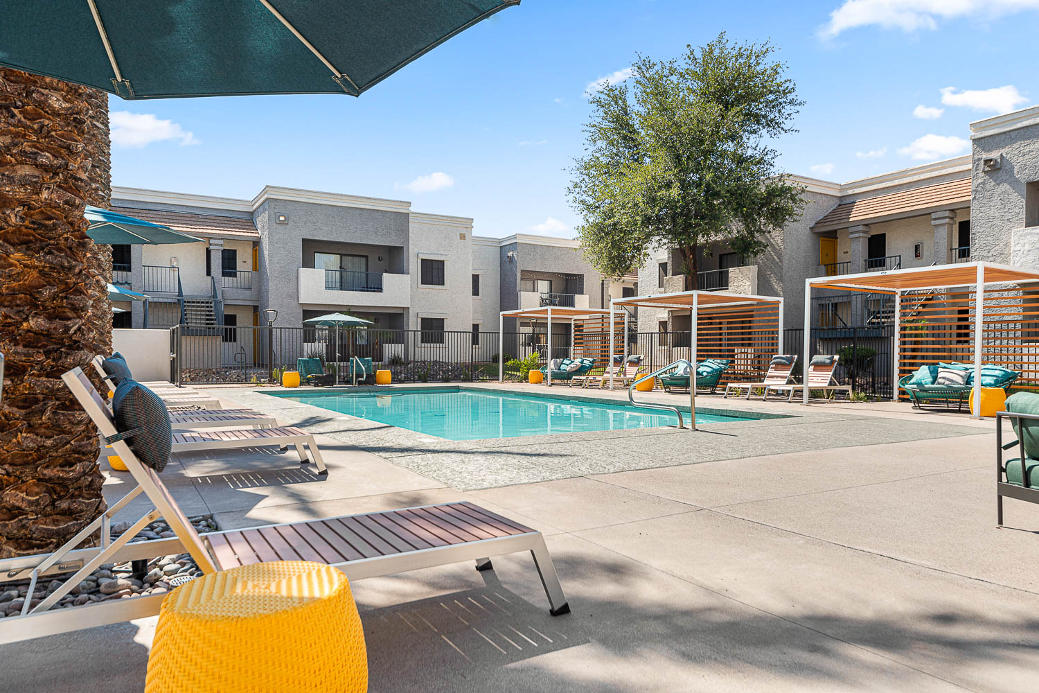 view of swimming pool from inside the fence, 3 semi covered cabanas ans seating chairs and lounge chairs