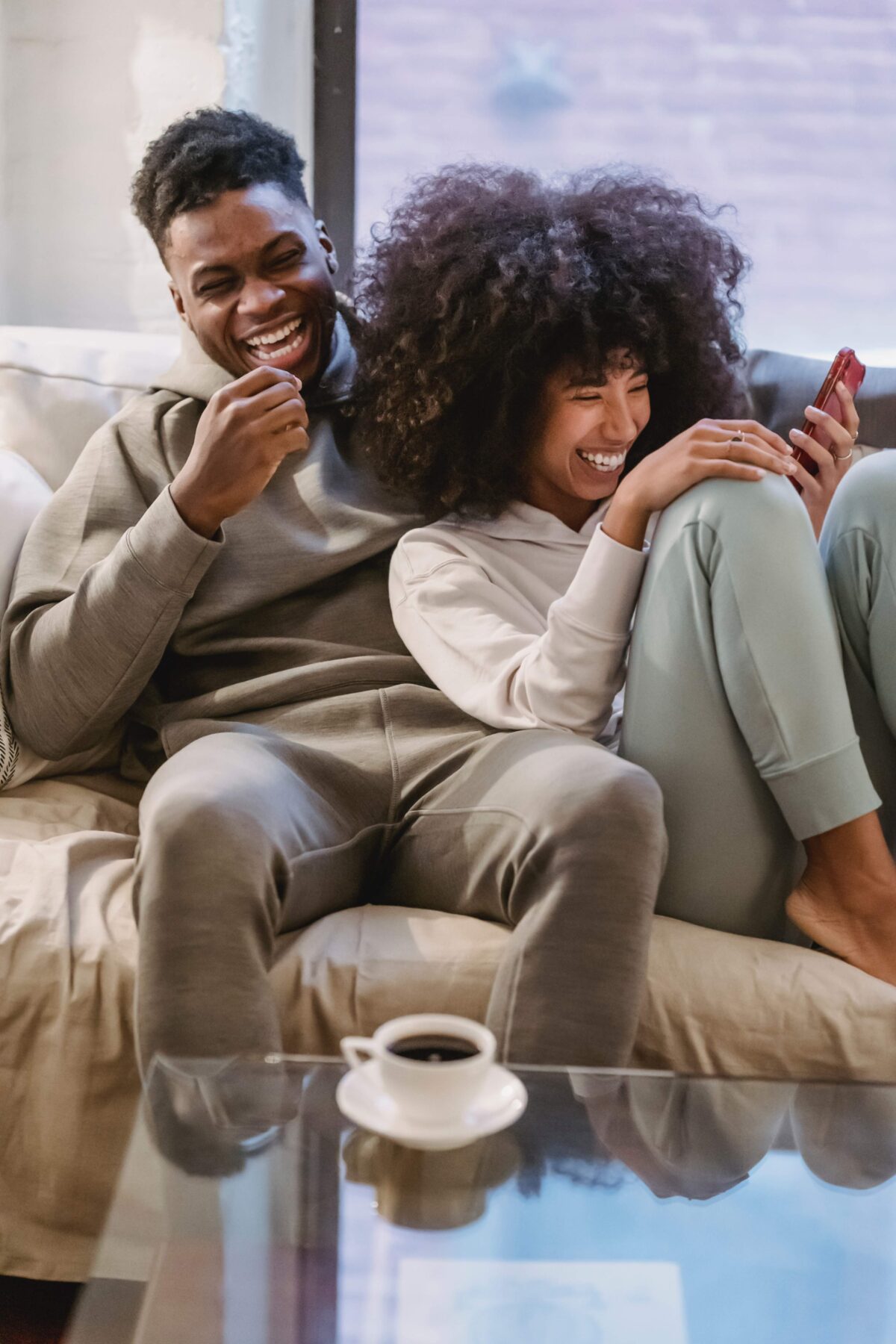 happy couple sitting on couch laughing at a phone with a cup of coffee on the table